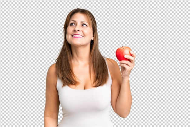 Middle age woman with an apple over isolated background looking up while smiling