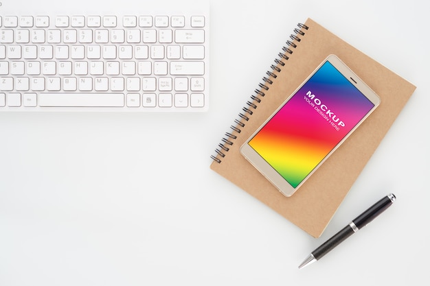 白のペンとコンピューターのキーボードを持つノートにスマートフォンの空白の画面をモックアップします。