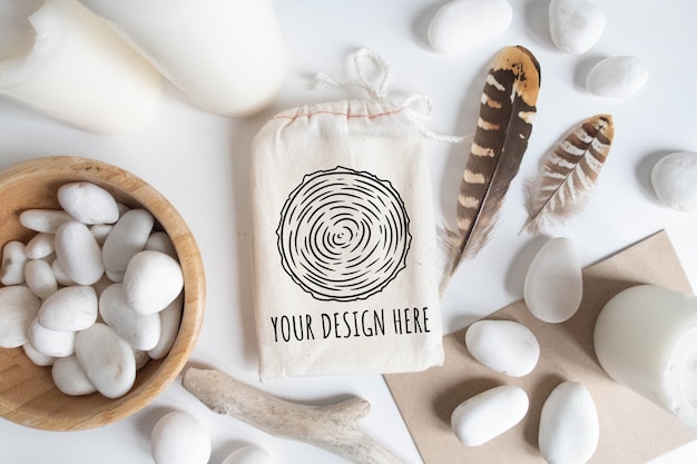 Mock up of cotton bag or pouch and bowl with white pebble and boho elements on white table.