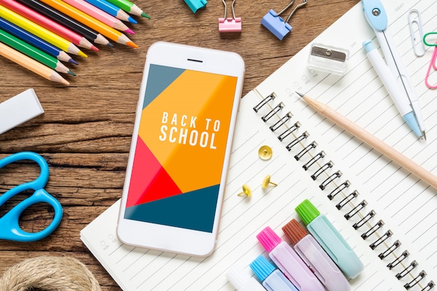 PSD mock up mobile phone with school stationary items on grunge wood