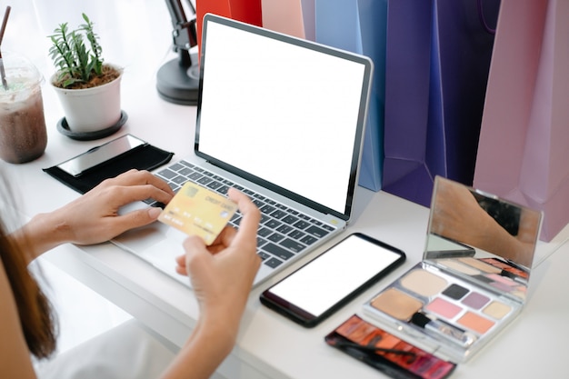 Modello di bella carta di credito della tenuta della donna che gode nel sito web di acquisto online con lo smartphone ed il computer portatile