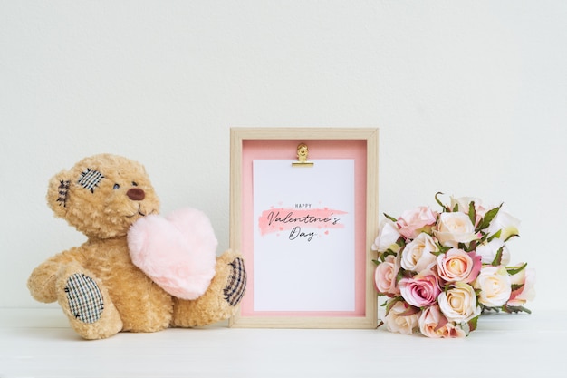 Mockup fotolijst en schattige beer met roze hart en boeket rozen.