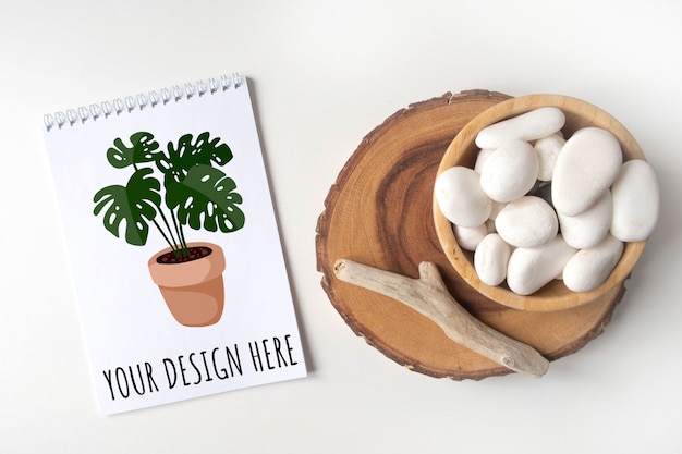 Mockup lege notebook lijst met een kom met witte kiezelsteen en boho rustieke decoraties op een witte tafel.