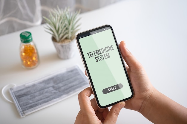 Макет мобильного телефона, человек, держащий смартфон с маской и медицинский планшет на столе для телемедицины