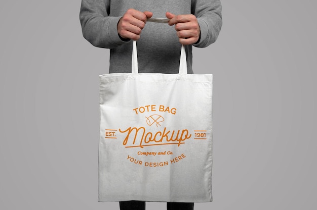 Mockup di modello che tiene una borsa tote su sfondo grigio