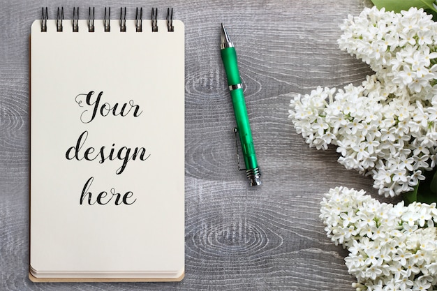 Mockup of spiral notebook on wooden table with flowers