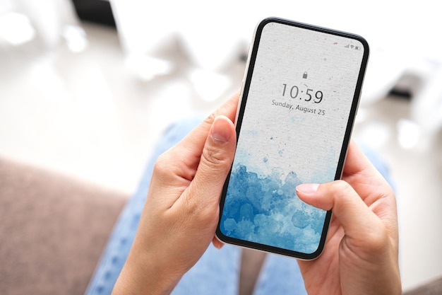 自宅のソファに空白の白い画面で黒いスマートフォンを持っているモックアップ女性の手。ビジネスと技術の概念