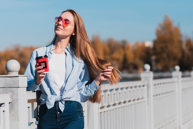 Ragazza bionda moderna che tiene un modello della tazza di caffè