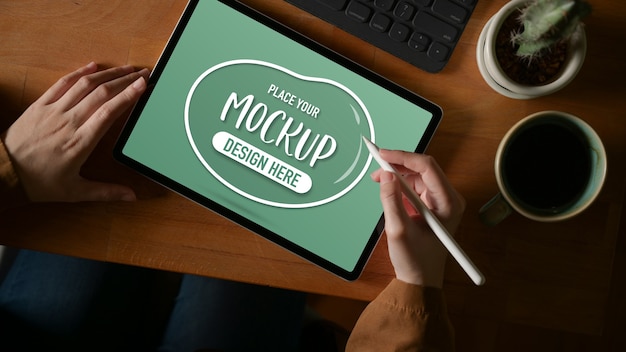 Overhead shot of female hands working on mock up tablet with stylus on wooden table