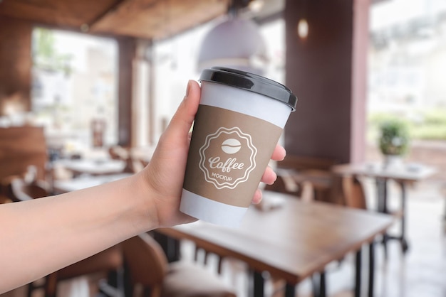 PSD paper cup mockup held in hand at a coffee shop