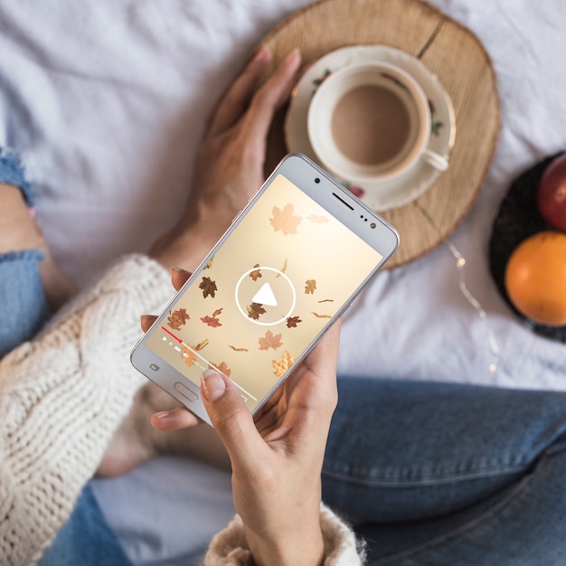 Person on bed looking at smartphone with autumn concept