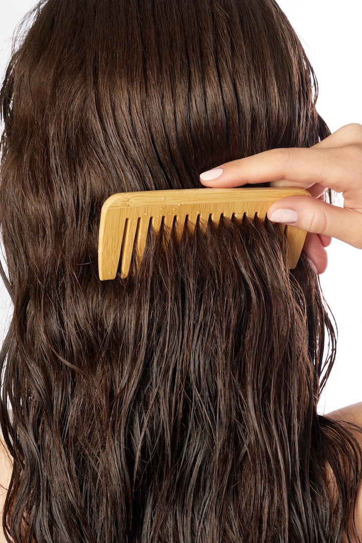 PSD a person is gently combing through wet dark brown hair using a widetooth bamboo comb