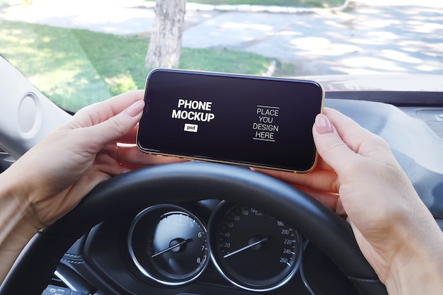 Phone in girl's hand on the steering wheel of a car mockup