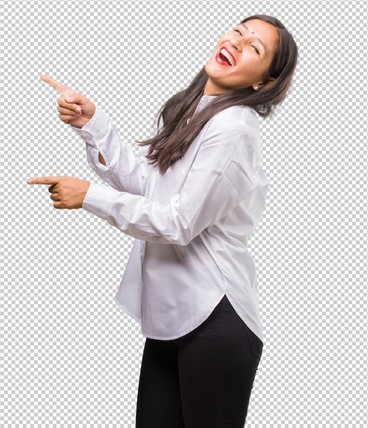 Portrait of a young indian woman pointing to the side, smiling surprised presenting something, natural and casual