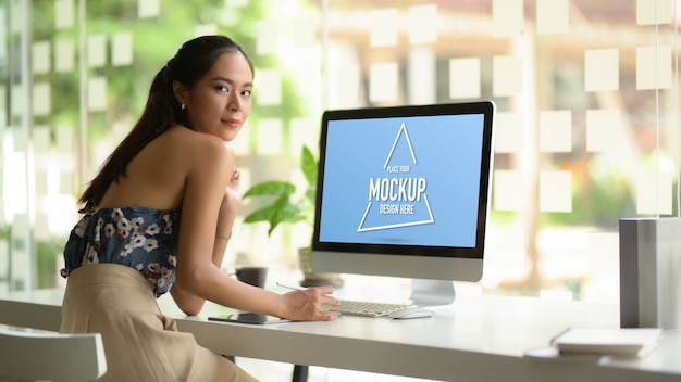 Portret żeński projektant mody patrząc do aparatu i uśmiechając się podczas pracy na stole komputera