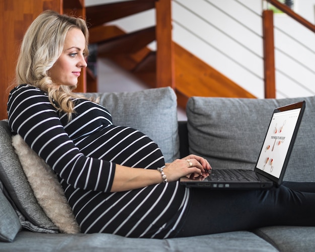 Беременная женщина на диване с помощью компьютера