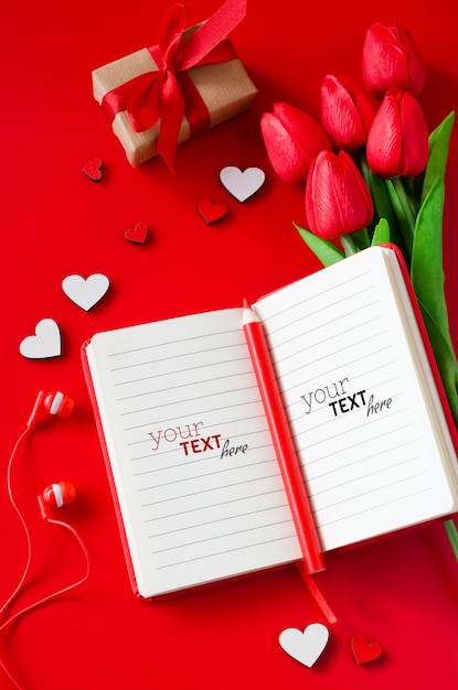 Red notebook with bouquet of tulips, gift box, wooden hearts, pencil and headphones.