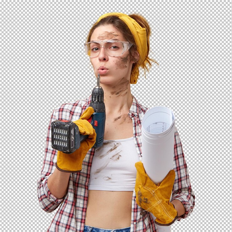 PSD selfconfident female builder wearing goggles white top and checkered shirt protective gloves holding drill and papers being dirty after hard work isolated over yellow wall maintenance