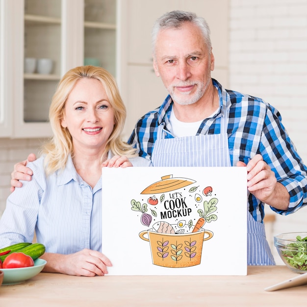 Senior couple in kitchen holding cardboard mock-up