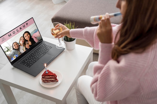 Vista laterale della donna che celebra a casa con gli amici su laptop e drink