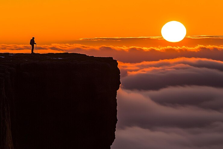 PSD silhouette of a hiker on a cliff overlooking a sea of clouds at sunset
