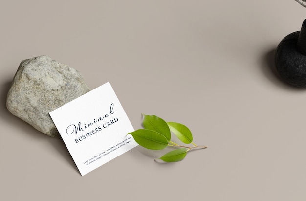 A small business card sits next to a rock and a plant.