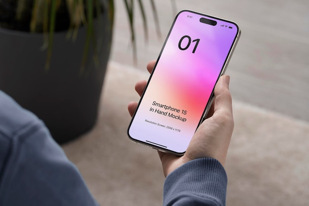 PSD smartphone 15 in mano con tappeto e pianta sullo sfondo