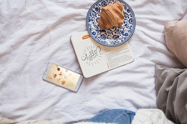 Smartphone op bed met dagboek en croissant