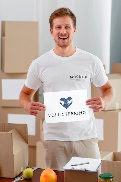 smiley male volunteer holding blank paper with food boxes for donation