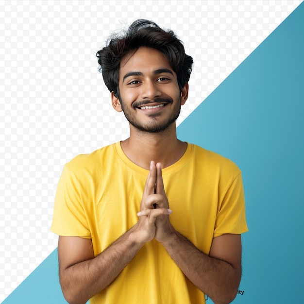 Smiling positive indian man wearing yellow shirt holding fingers crossed while standing isolated over blue studio wall