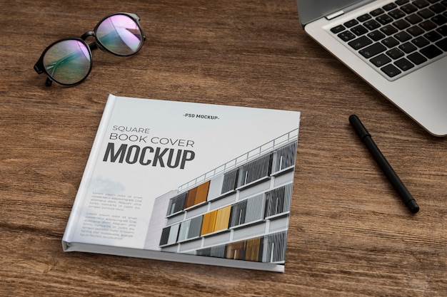 PSD square book mock-up on wooden office desk with laptop and eyeglasses