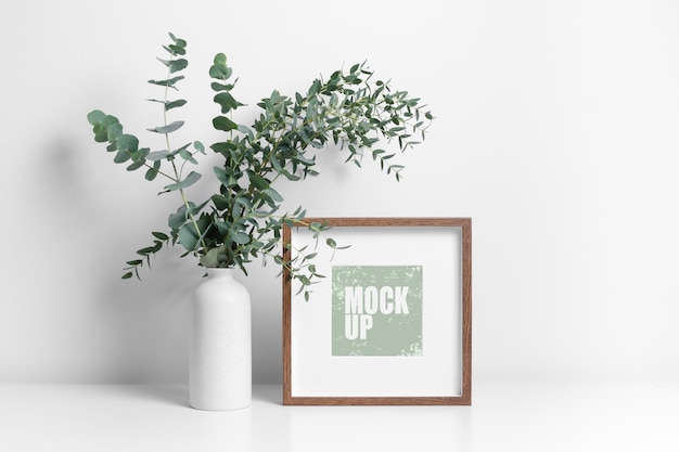 Square frame mockup with fresh eucalyptus plant in white room interior