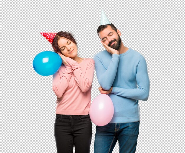 Stel met ballons en verjaardagshoeden die slaapgebaar maken. Schattig zoete uitdrukking