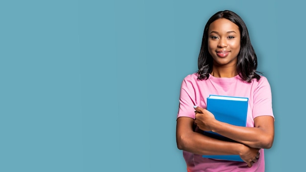 A student in a pink shirt holds a blue folder and smiles