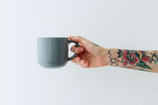 Tattooed hand holding a graysih blue coffee cup 