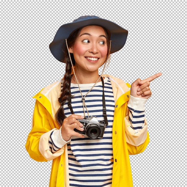 Tevreden Koreaanse vrouw draagt hoofddoek gestreepte trui en gele regenjas wijst wijsvinger opzij promoot kopie ruimte draagt retro camera reist in wilde plaats heeft avontuurlijke expeditie