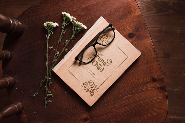 Top view of book on chair with flowers and glasses