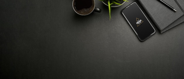 PSD top view of dark workspace with smartphone mockup, stationery and cup