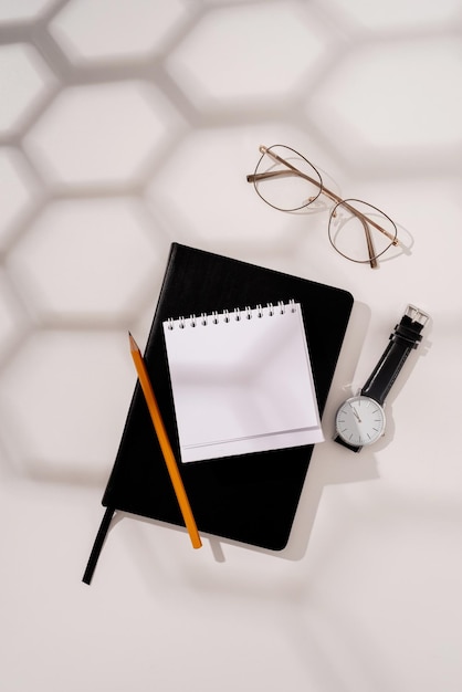 Top view desk arrangement. Time management, planning concept. Minimal style blank calendar for mock up, notebook, trendy glasses, watch and pencil on white backdrop, shadow overlay