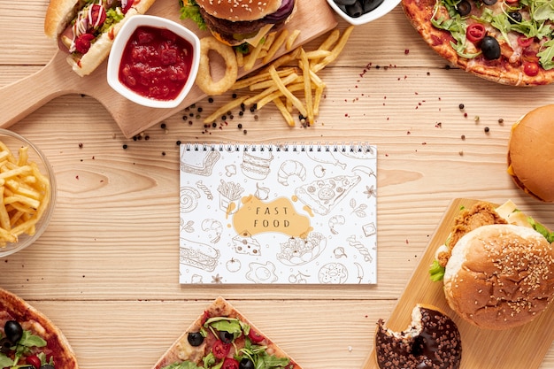 Top view of fast food on wooden table with notebook mock-up