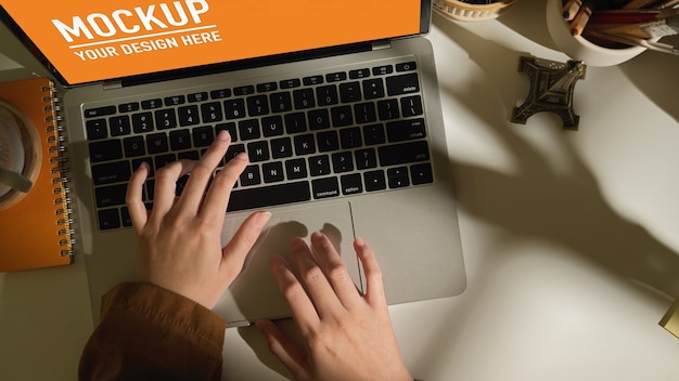 Top view of female hands typing on laptop mockup on white worktable in home office room