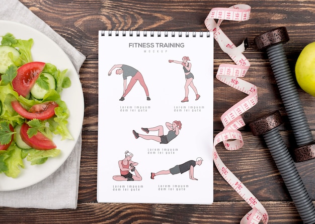 Top view of fitness notebook with measuring tape and weights