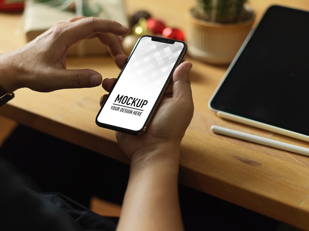 Vista dall'alto della mano che tiene il mockup dello smartphone e le decorazioni di natale