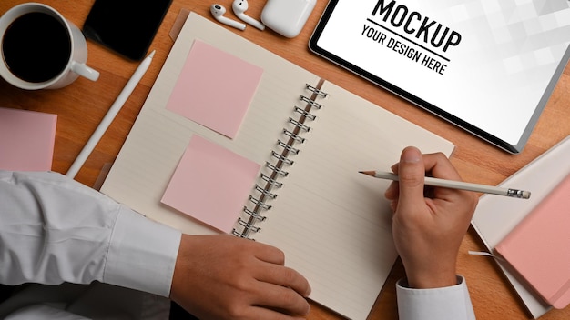 top view of male hand holding schedule book and coffee cup with tablet mockup
