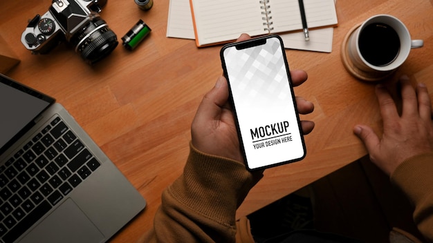 Top view of male hand holding smartphone mockup on worktable