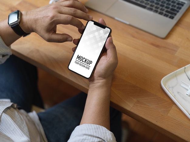 PSD top view of male hands using smartphone mockup on wooden worktable with laptop