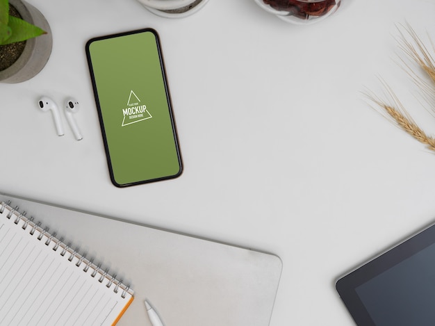 Top view of mock up smartphone on worktable with notebook, earphone and supplies