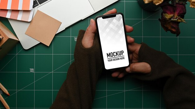 ワークスペースでスマートフォンのモックアップを持っている男性の手の上面図