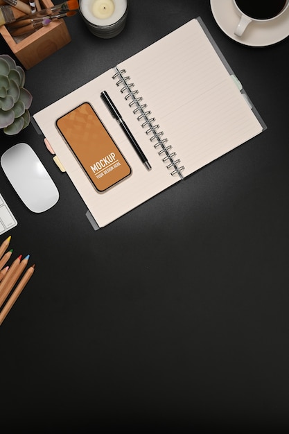 Top view of workspace with blank notebook, stationery, smartphone mockup