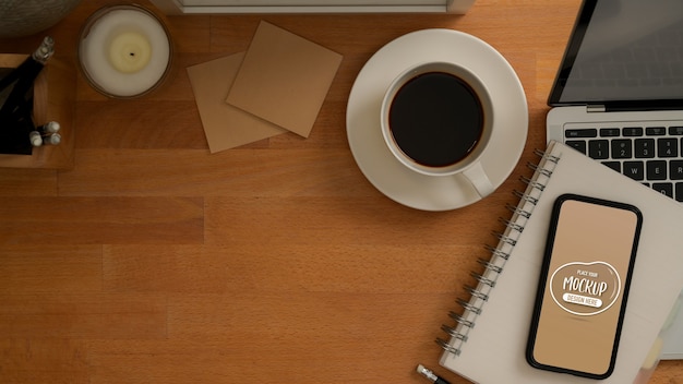 Vista dall'alto del piano di lavoro con mock up di smartphone, laptop, tazza di caffè, cancelleria e spazio di copia